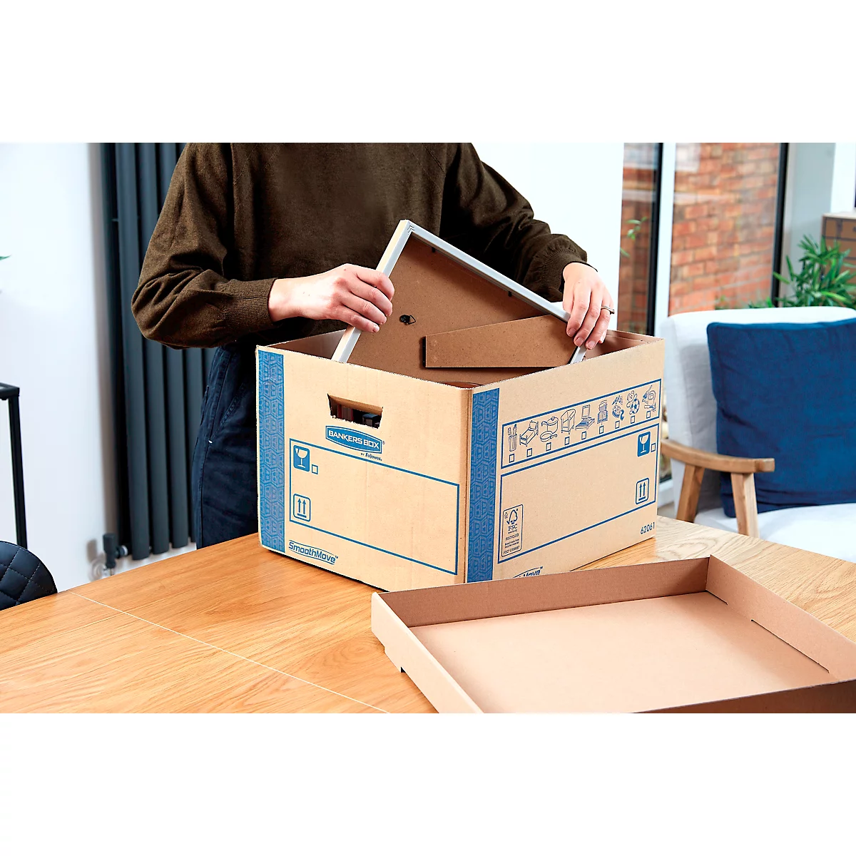 Person legt einen weissen Bilderrahmen in eine braune Archivbox. Vorne liegt eine leere Box.