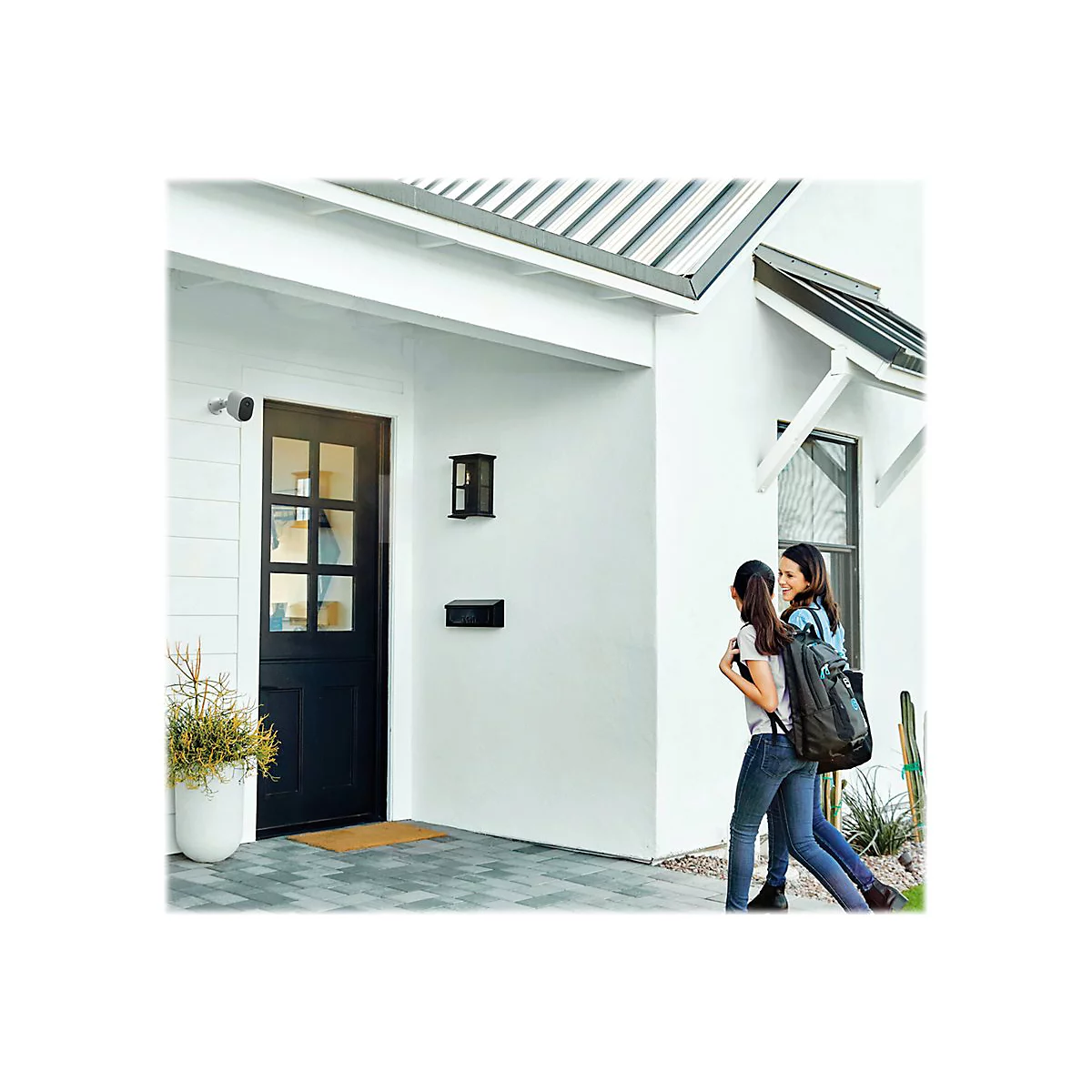 Zwei Frauen gehen auf ein Haus zu, an der Hauswand ist eine Überwachungskamera angebracht.