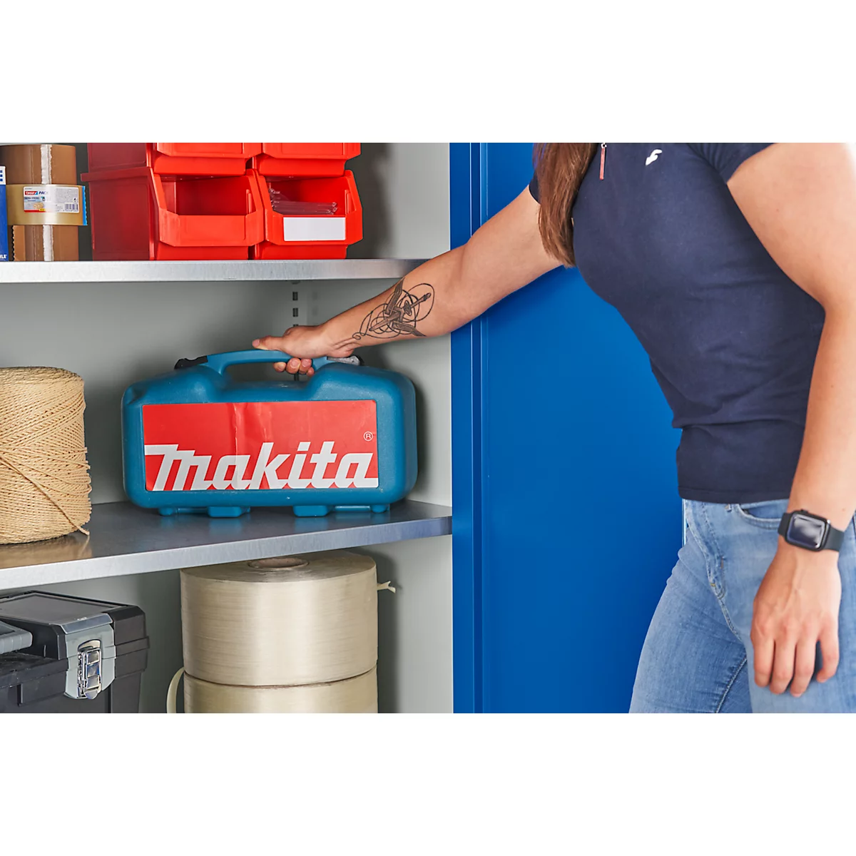 Persona tomando una caja de herramientas Makita azul de un estante de metal.