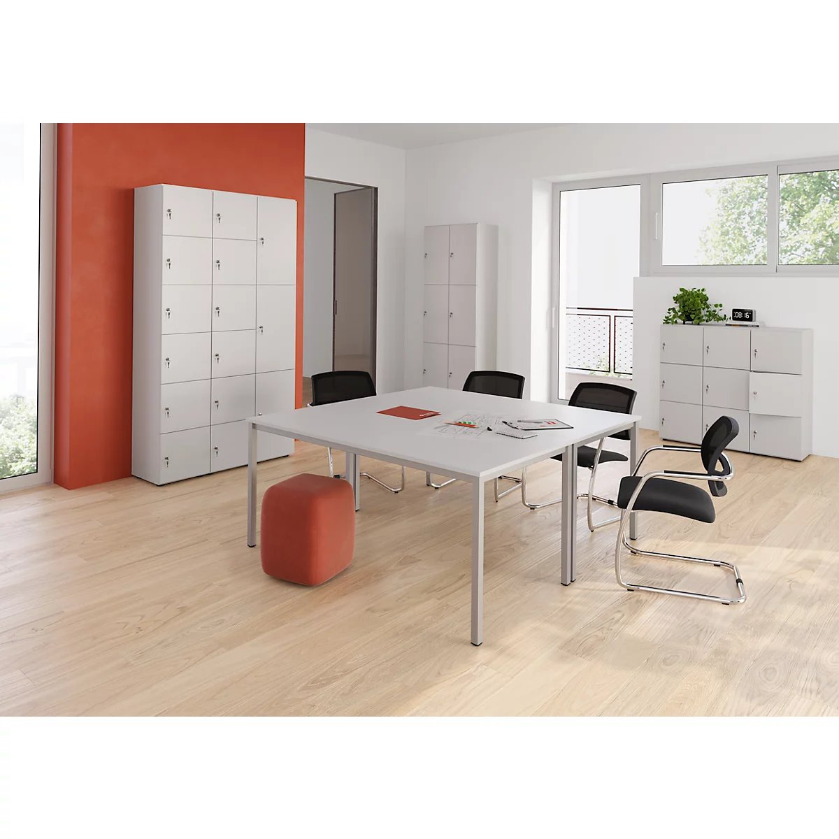 Un bureau lumineux avec une table blanche, des chaises noires, des armoires, un mur rouge et un pouf orange.