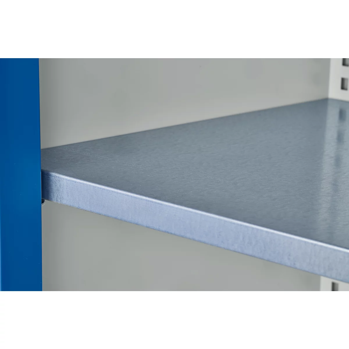 Gros plan sur une étagère en métal argenté avec un support latéral bleu contre un mur gris clair.