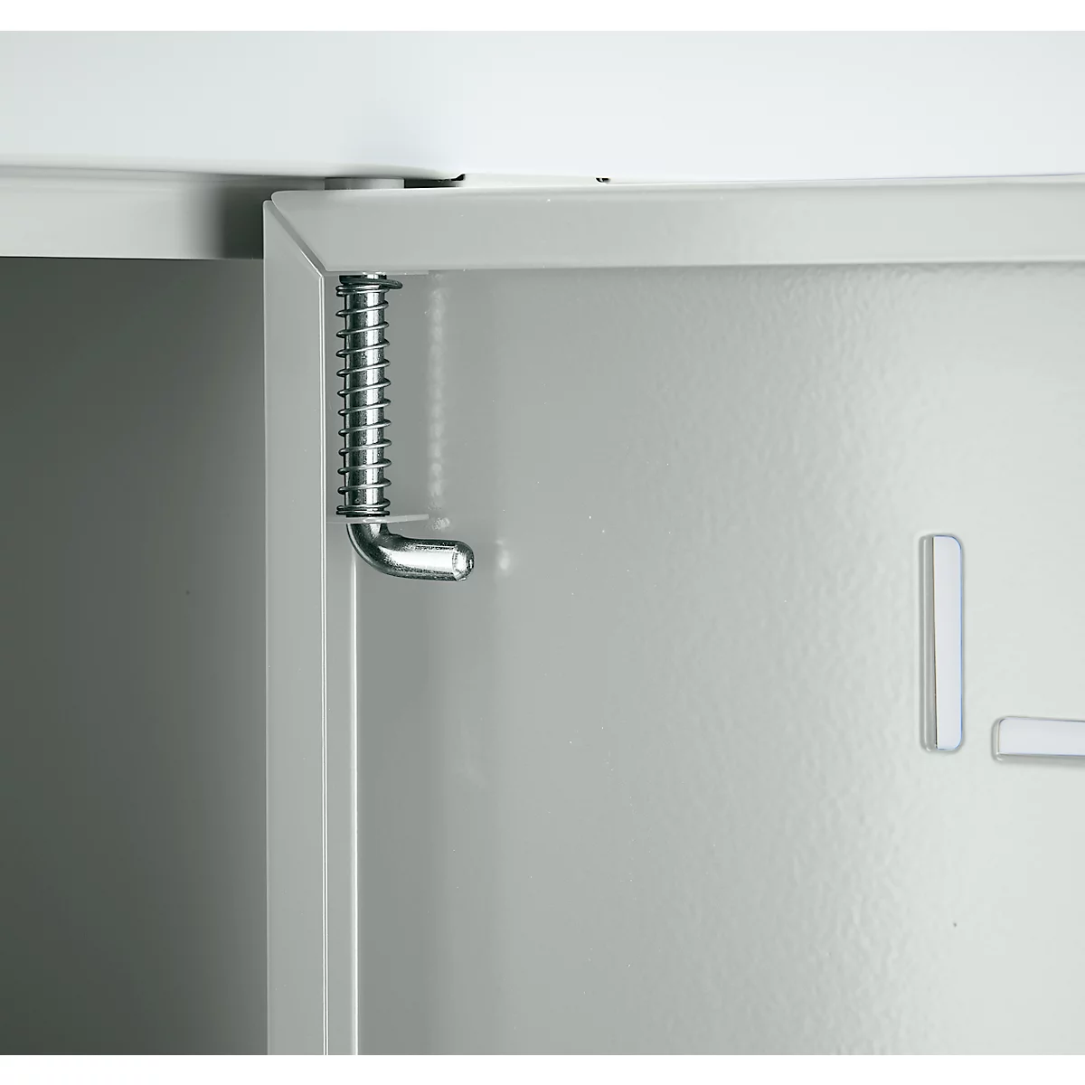 Gros plan sur une charnière de porte d'armoire avec ressort. La porte est gris clair, la charnière métallique.