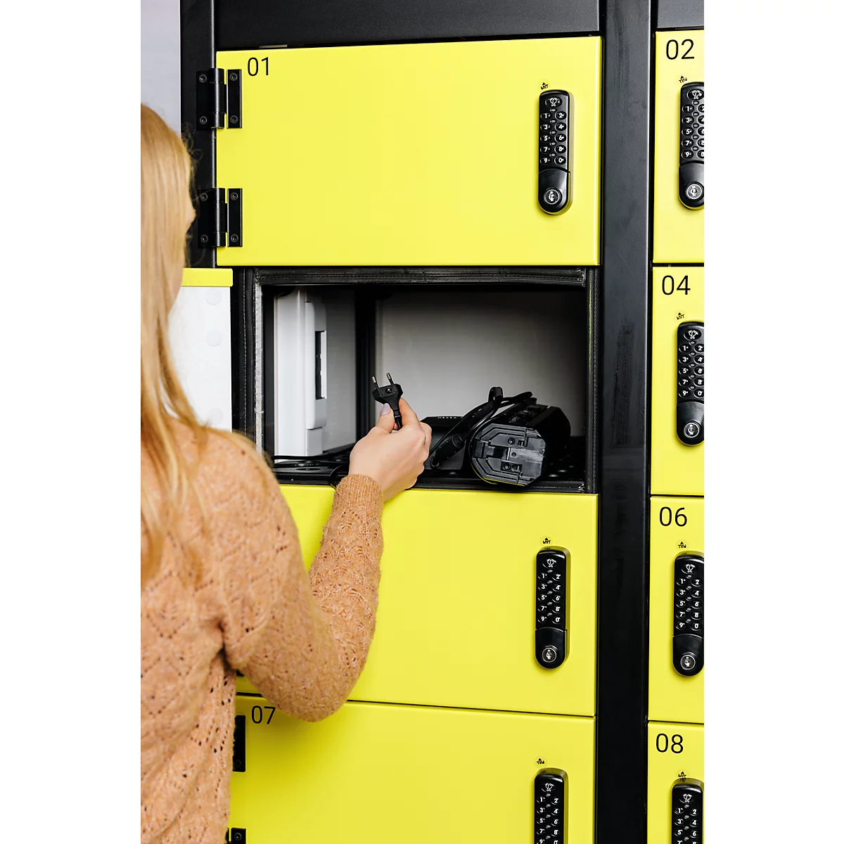 Une femme ouvre un casier jaune pour en sortir quelque chose. Il y a un clavier sur le casier pour entrer les chiffres.