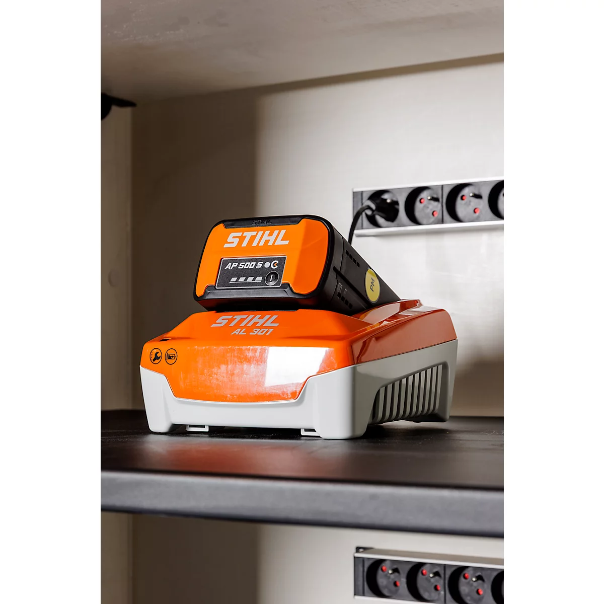 Batterie orange et noire de Stihl avec station de charge. Le dessus indique Stihl AP 500 S C.