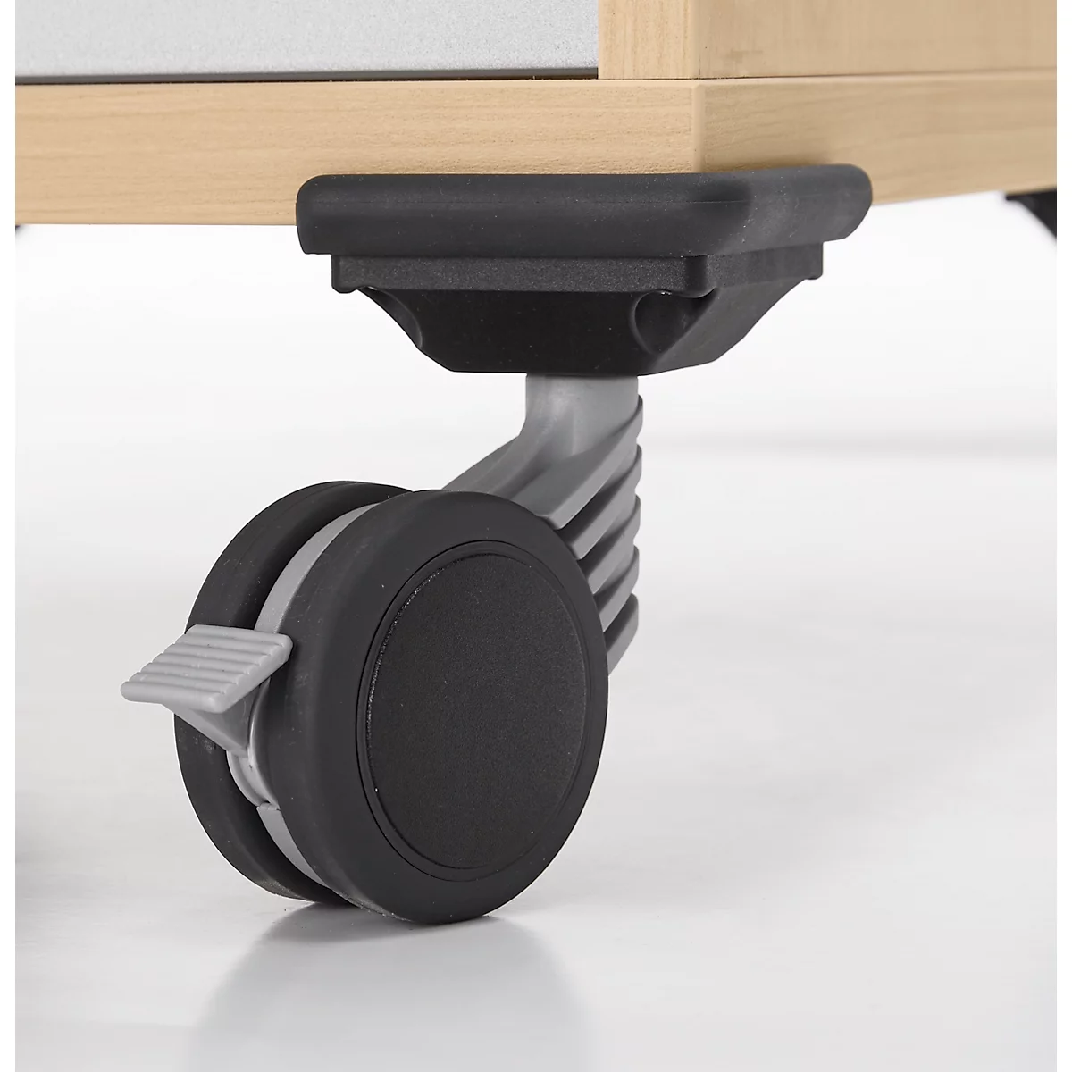 Gros plan d'un pied de roulette fixé sous un meuble en bois clair. Le pied est en plastique noir avec un levier de verrouillage gris.