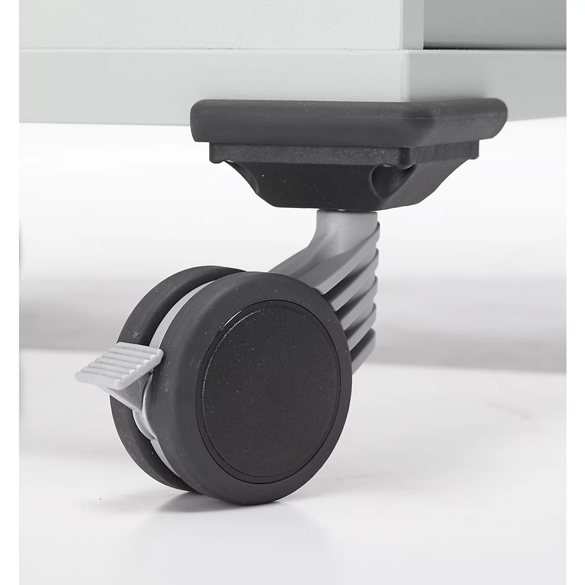 Gros plan d'une roulette : Roue noire avec levier de blocage sur un meuble gris.