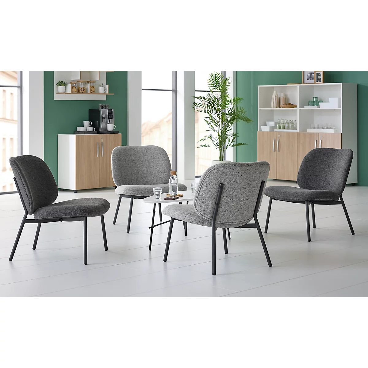 Four gray chairs surround a small table with glasses and a water bottle. Cabinets in the background.