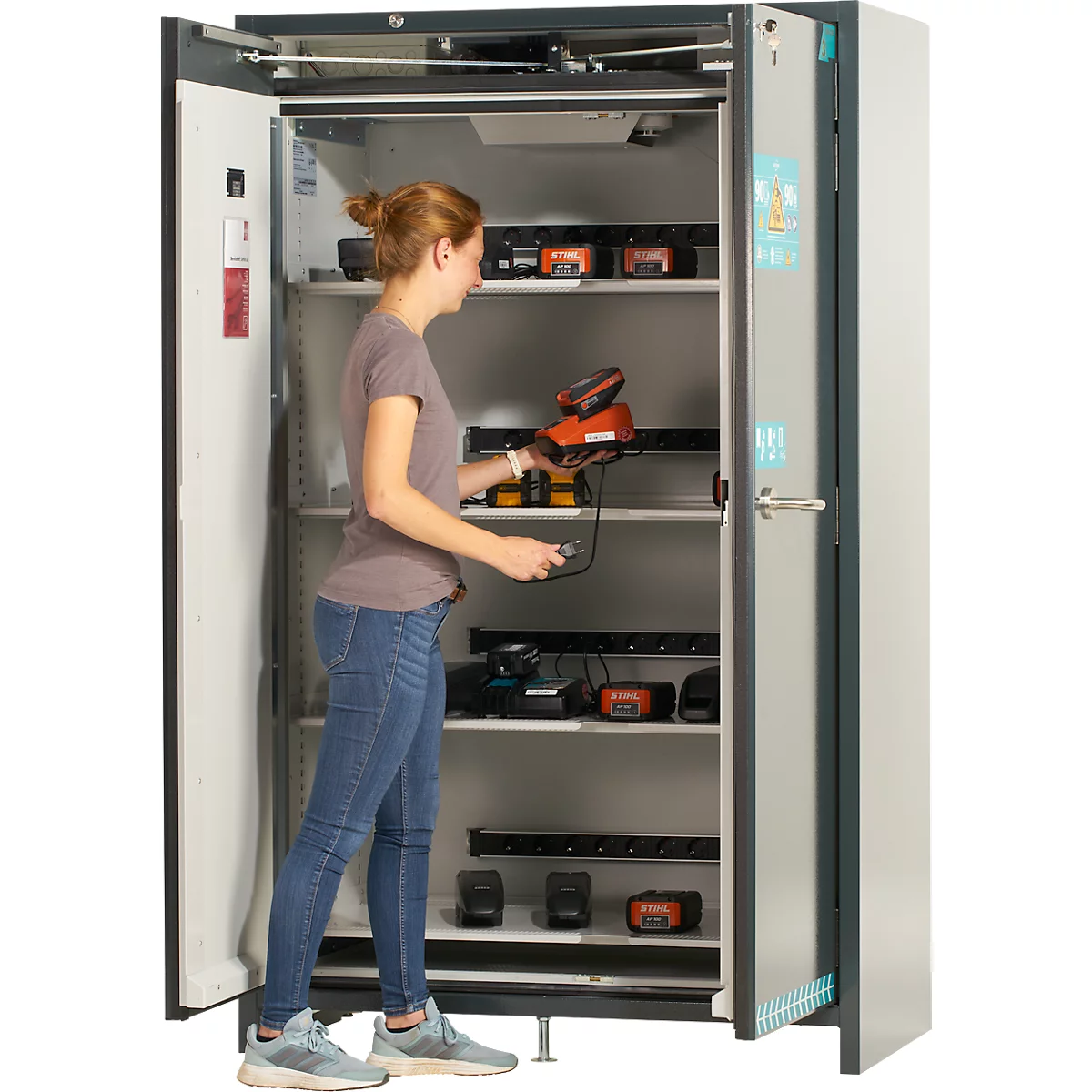 Eine Frau öffnet einen Schrank mit Werkzeug, in dem sich aufgeladene Werkzeuge befinden.