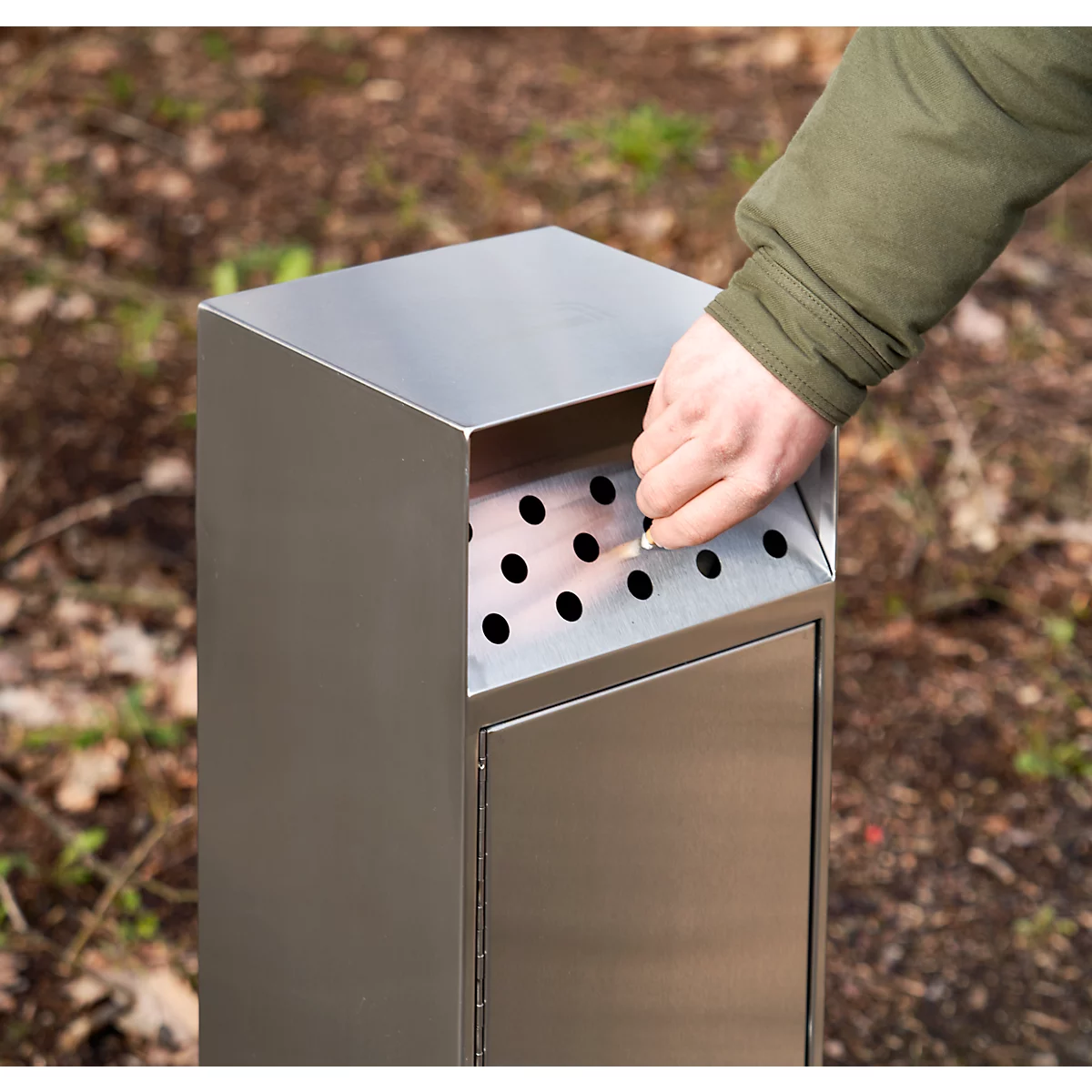 Person putting a cigarette in a metal ashtray standing outdoors.