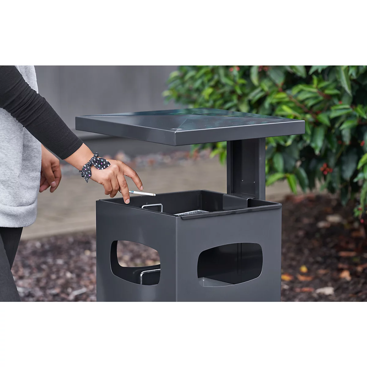 Person drops a cigarette into a black ashtray. The hand with bracelet is in focus.