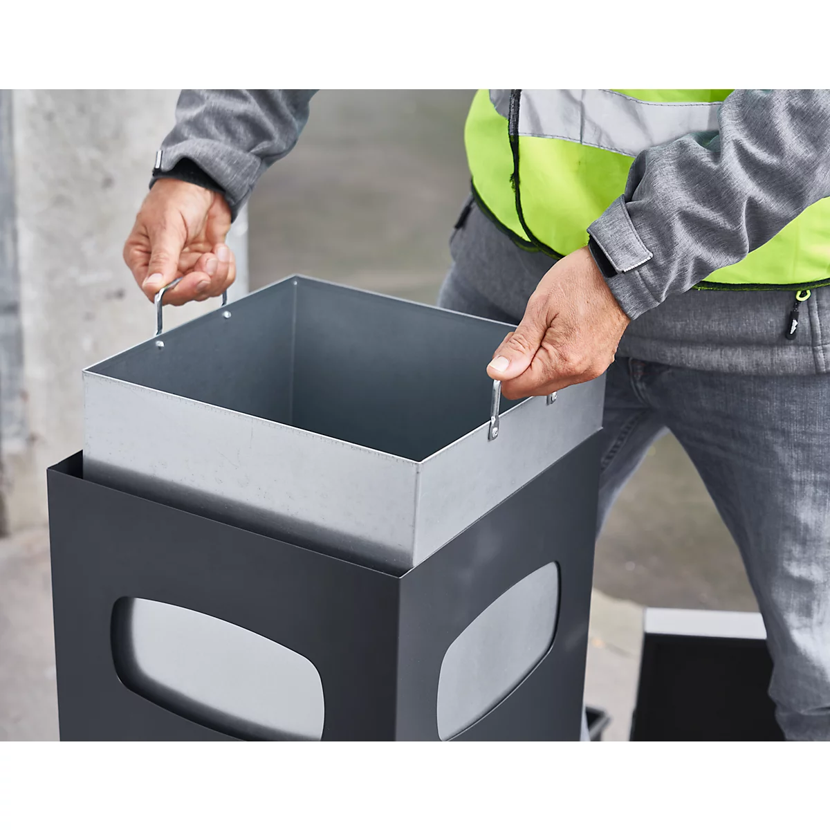 Person holding a removable metal container above a grey waste container.