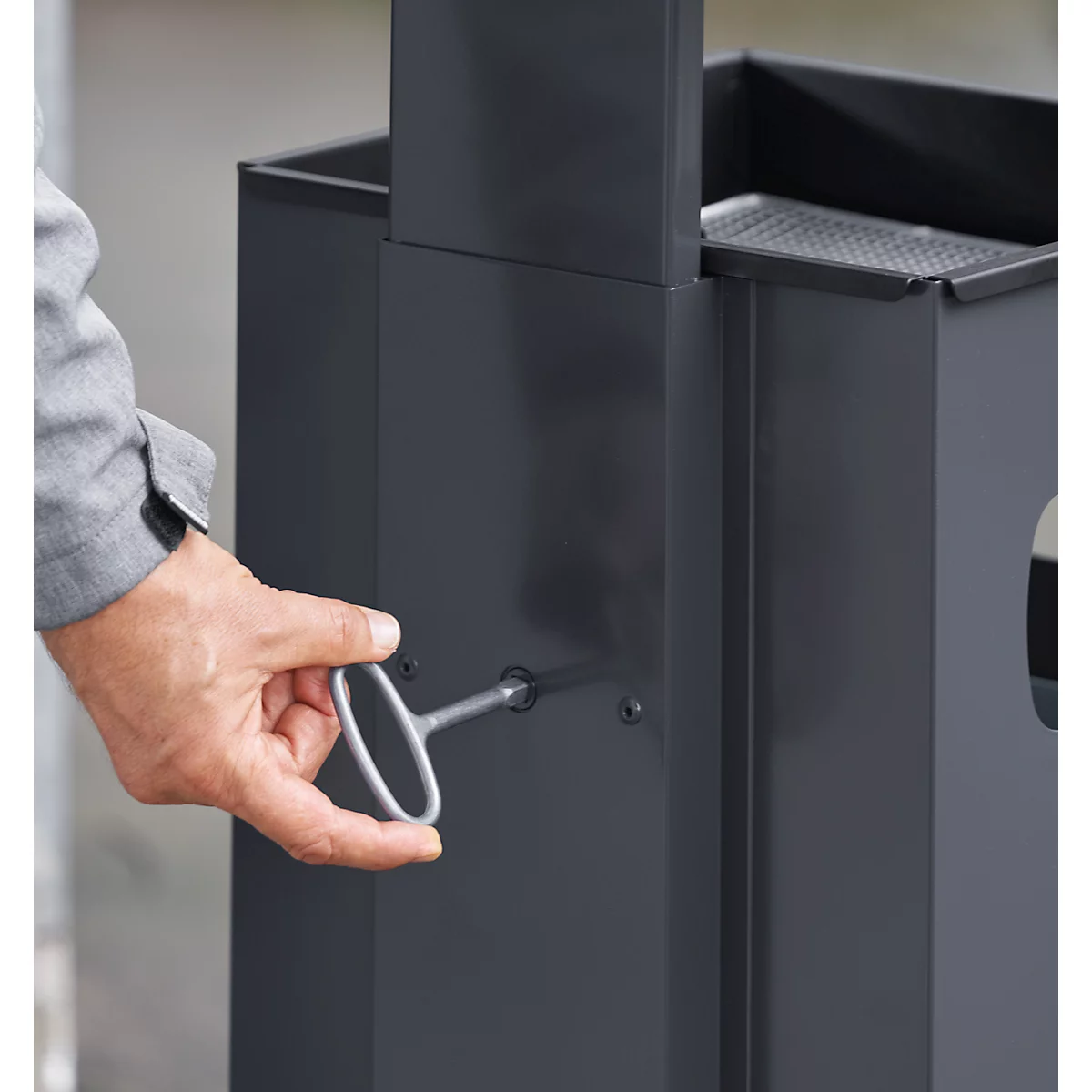 A hand operates a key on a gray metal container.