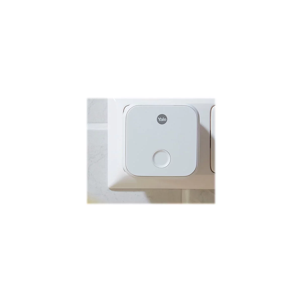 Ein weißer, quadratischer Yale WLAN-Bridge-Adapter eingesteckt in einer Wandsteckdose.