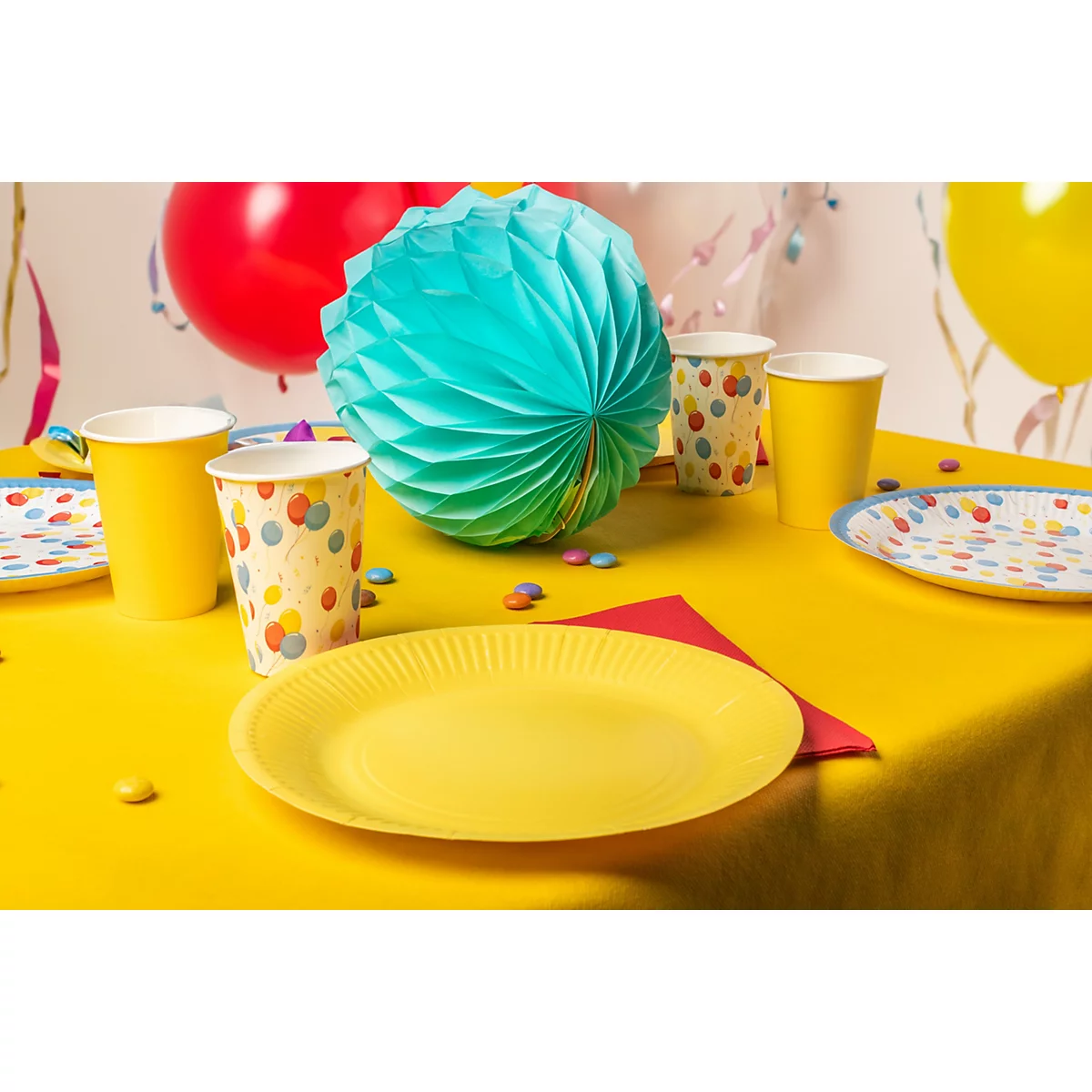 Table jaune avec ballons, assiettes, tasses et décoration. Tout pour une fête.