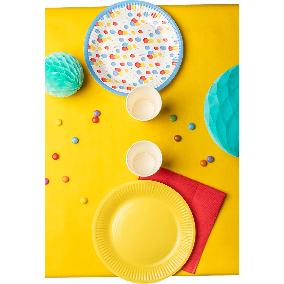 Table jaune avec décorations de fête : assiettes, gobelets, serviettes, confettis et guirlandes.