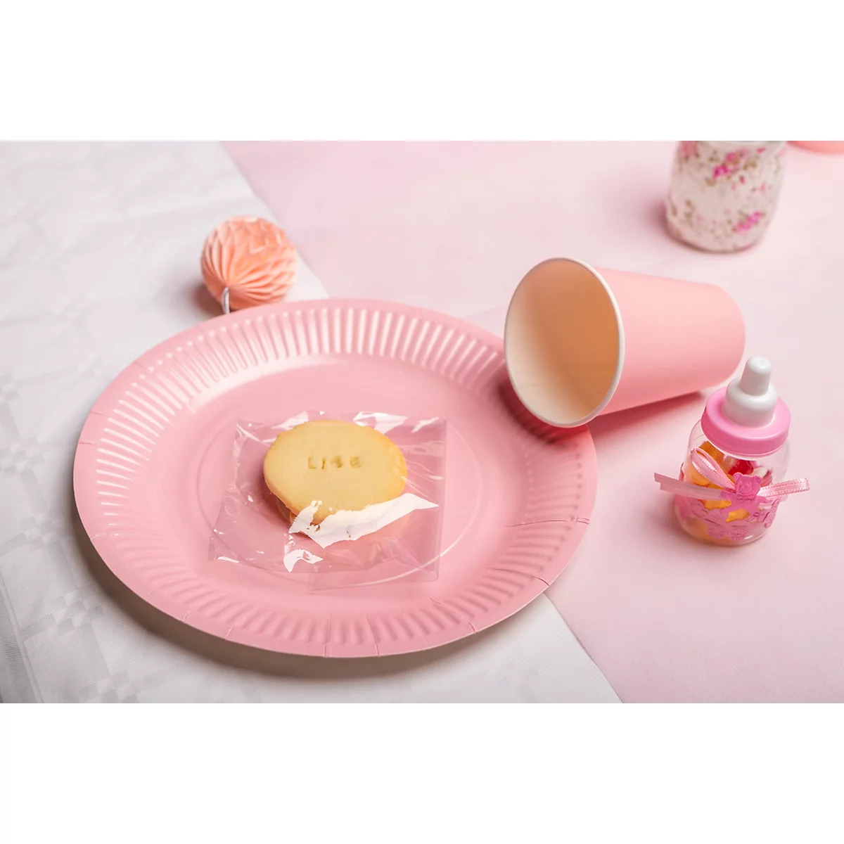 Une assiette rose avec des biscuits, une tasse et des biberons. Le biscuit est emballé dans du papier d'aluminium et porte le nom de "Lisa".