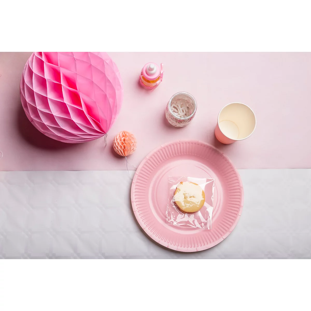 Vue aérienne d'une décoration de table rose. Un cookie dans du papier d'aluminium sur une assiette, à côté de tasses, de décorations.
