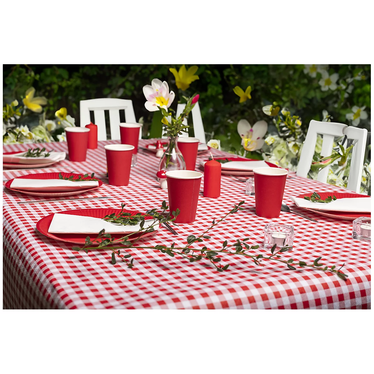 Une table de pique-nique dressée avec une nappe à carreaux rouge et blanc, des gobelets en papier rouges, des assiettes, des serviettes et un vase de fleurs.