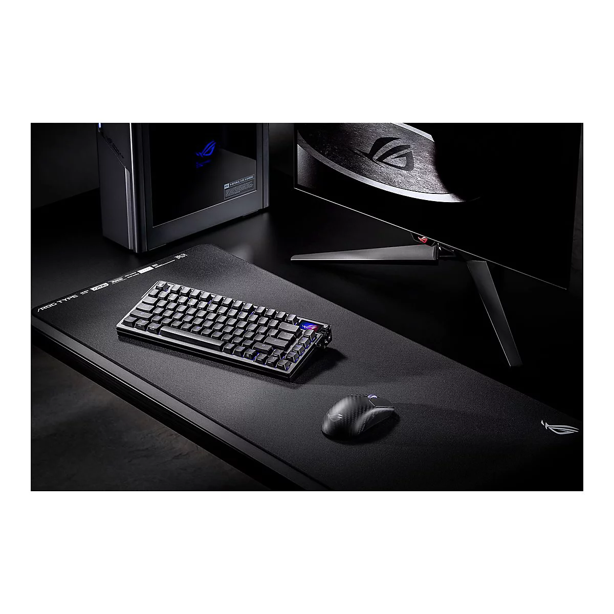 Schwarze Gaming-Tastatur, Maus und Monitor auf dunkler Tischplatte. Leuchtende blaue Tasten und ein ROG-Logo sind erkennbar.