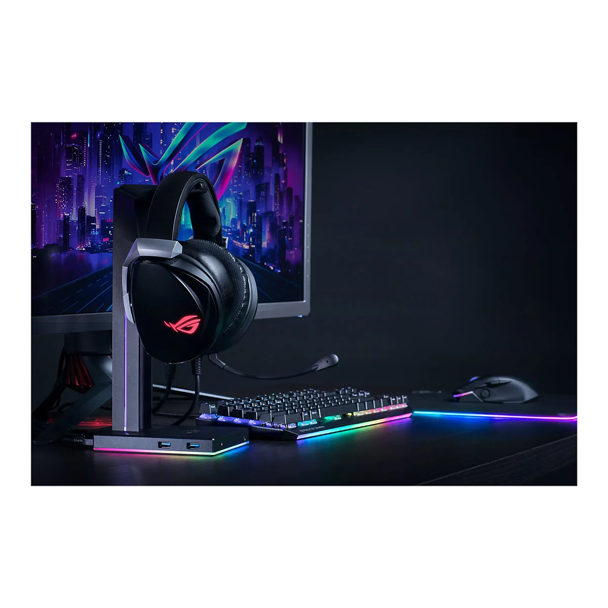 Schwarzes Gaming-Headset mit Mikrofon auf Halterung, leuchtende Tastatur, Maus, Bildschirm.