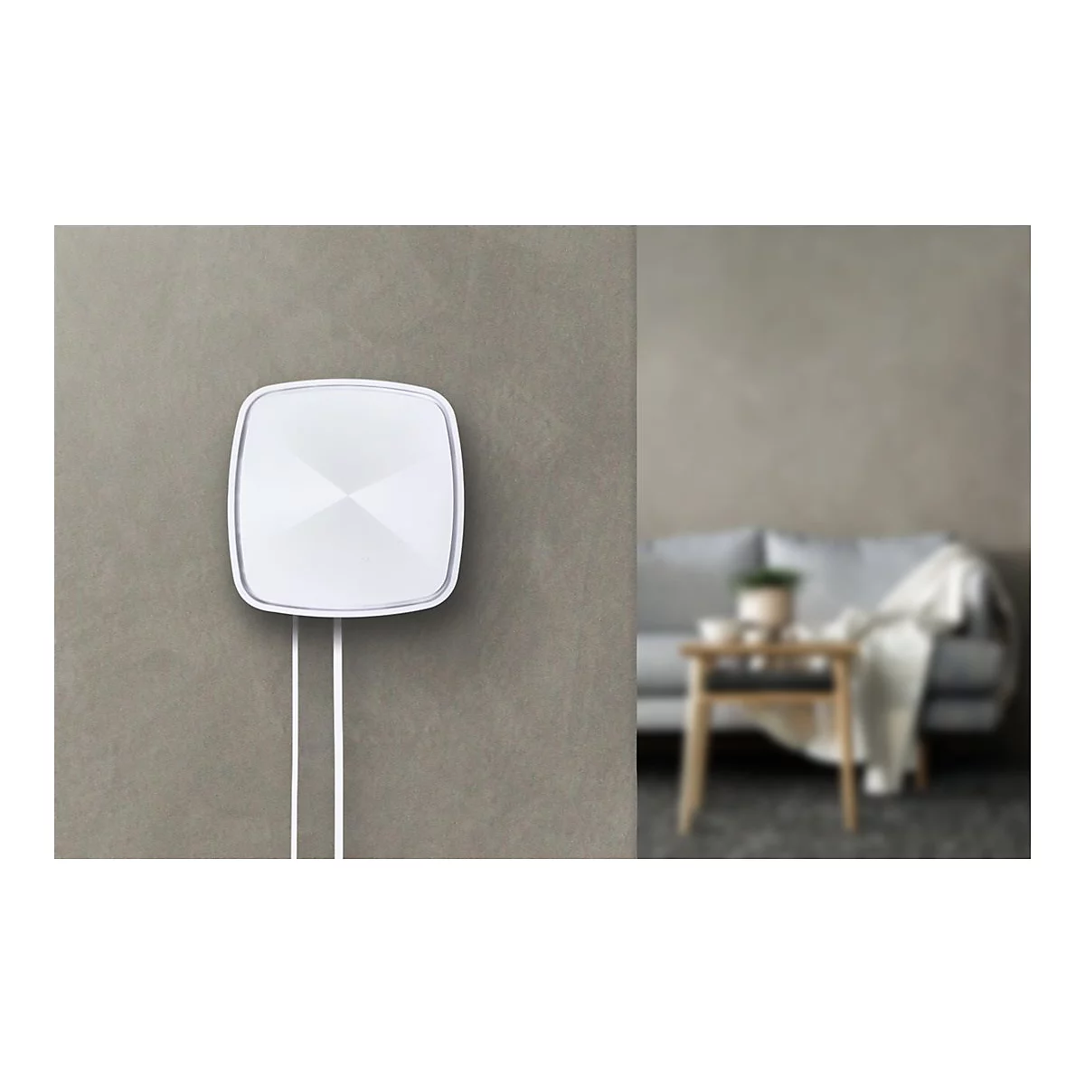 WeiÃŸes, quadratisches GerÃ¤t an grauer Wand, darunter zwei Kabel. Im Hintergrund verschwommenes Wohnzimmer.