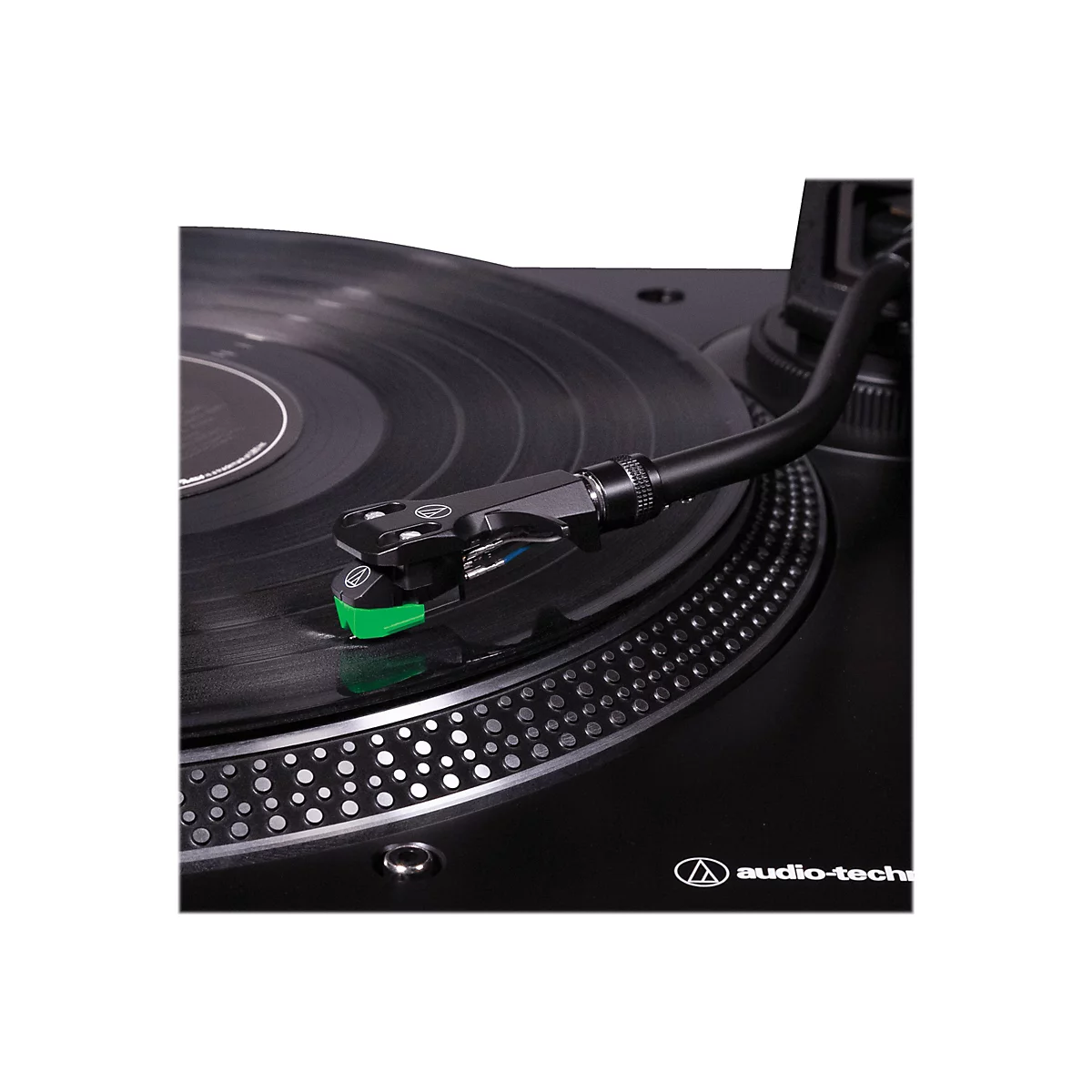 Nahaufnahme eines Plattenspielers mit schwarzem Tonarm und grünem Tonabnehmer auf einer Vinylplatte.