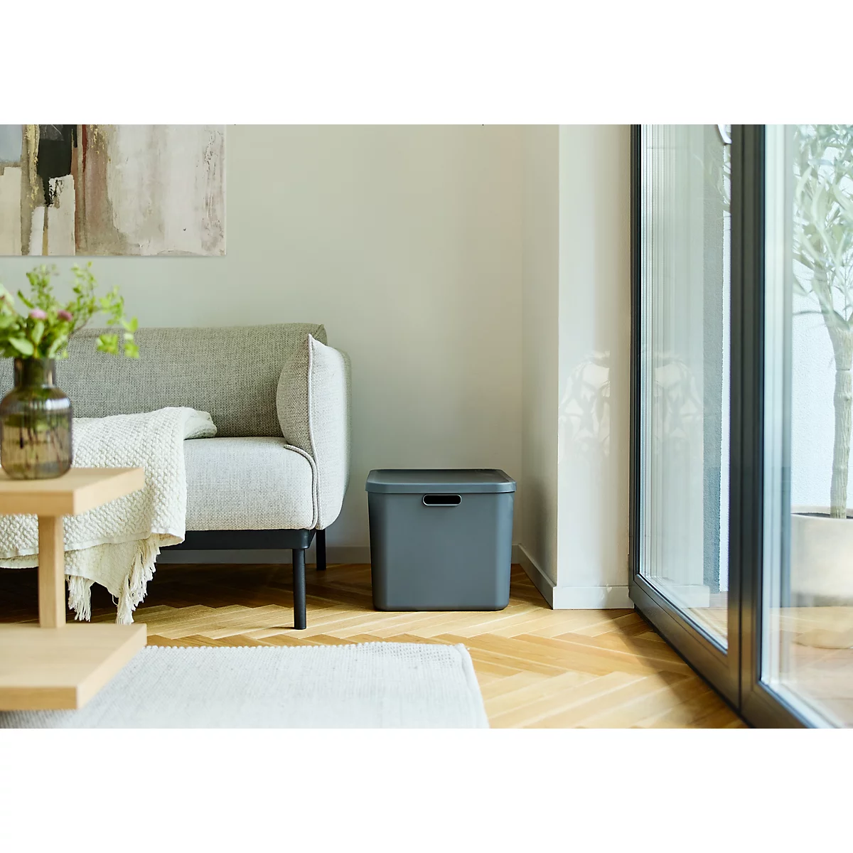 Graue Aufbewahrungsbox in einem Wohnzimmer neben einem Sofa.
