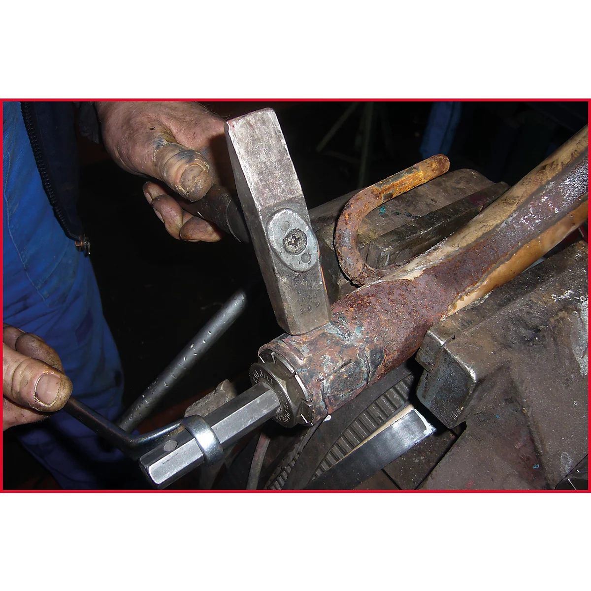 Eine Hand hält einen Hammer, ein Schraubenschlüssel wird auf ein Metallteil in einem Schraubstock geschraubt.