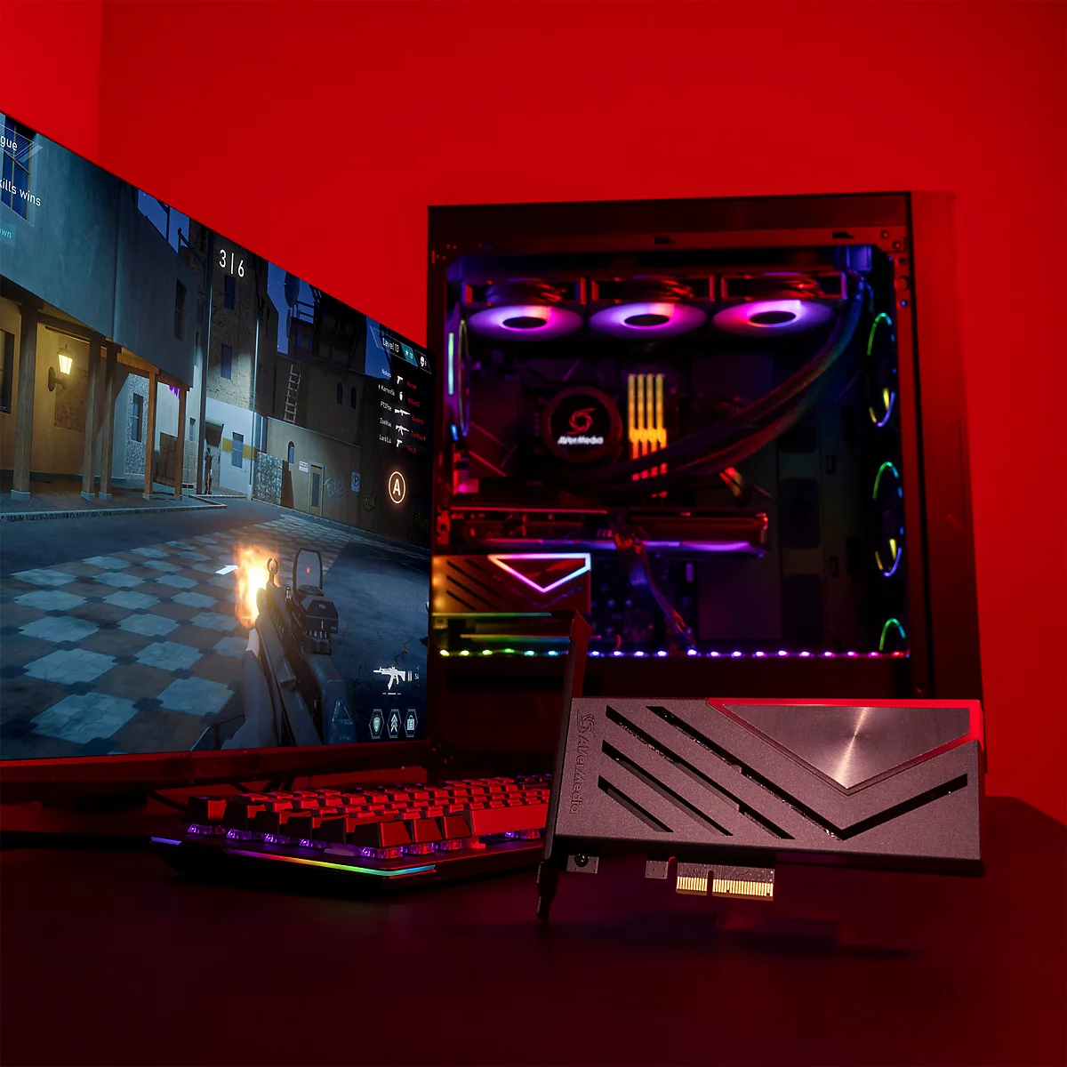 Eine AVerMedia Capture Card liegt auf einem Tisch vor einem leuchtenden Gaming-PC und einem Monitor.