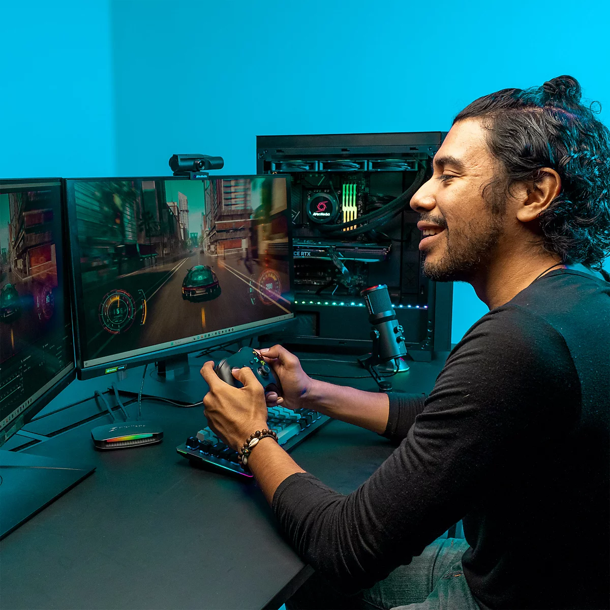 Ein junger Mann mit Dutt spielt lächelnd ein Videospiel an einem Gaming-PC mit zwei Monitoren und RGB-Beleuchtung.