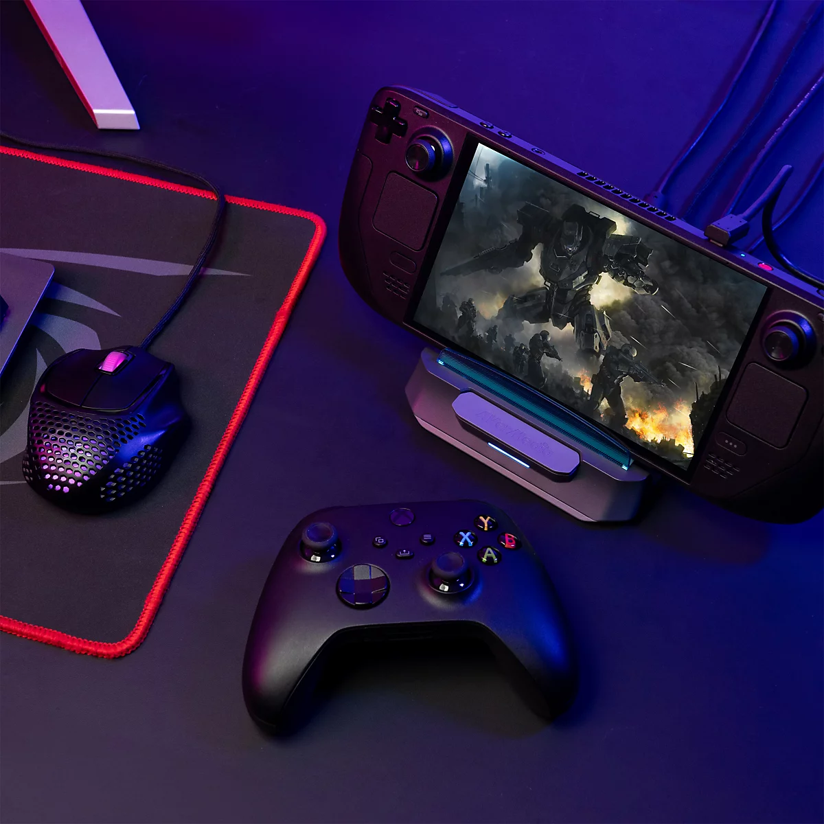 Handheld-Konsole in Dockingstation auf Schreibtisch mit Controller und Maus, beleuchtet durch blaues Licht.