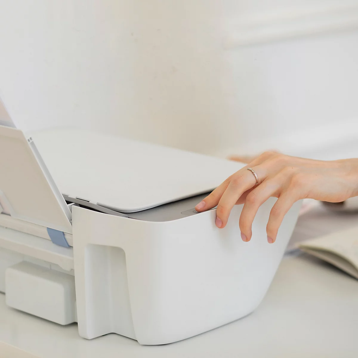 Une main faisant fonctionner une imprimante de bureau blanche.