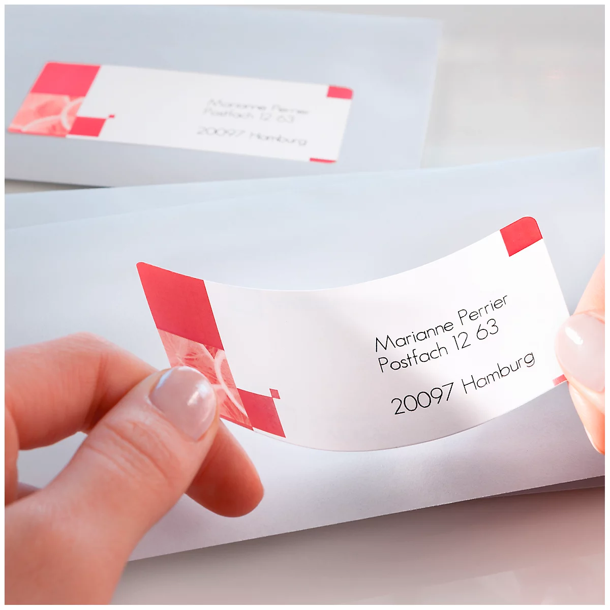 A hand peeling an address label from a white envelope. The label has a name and address with red accents.