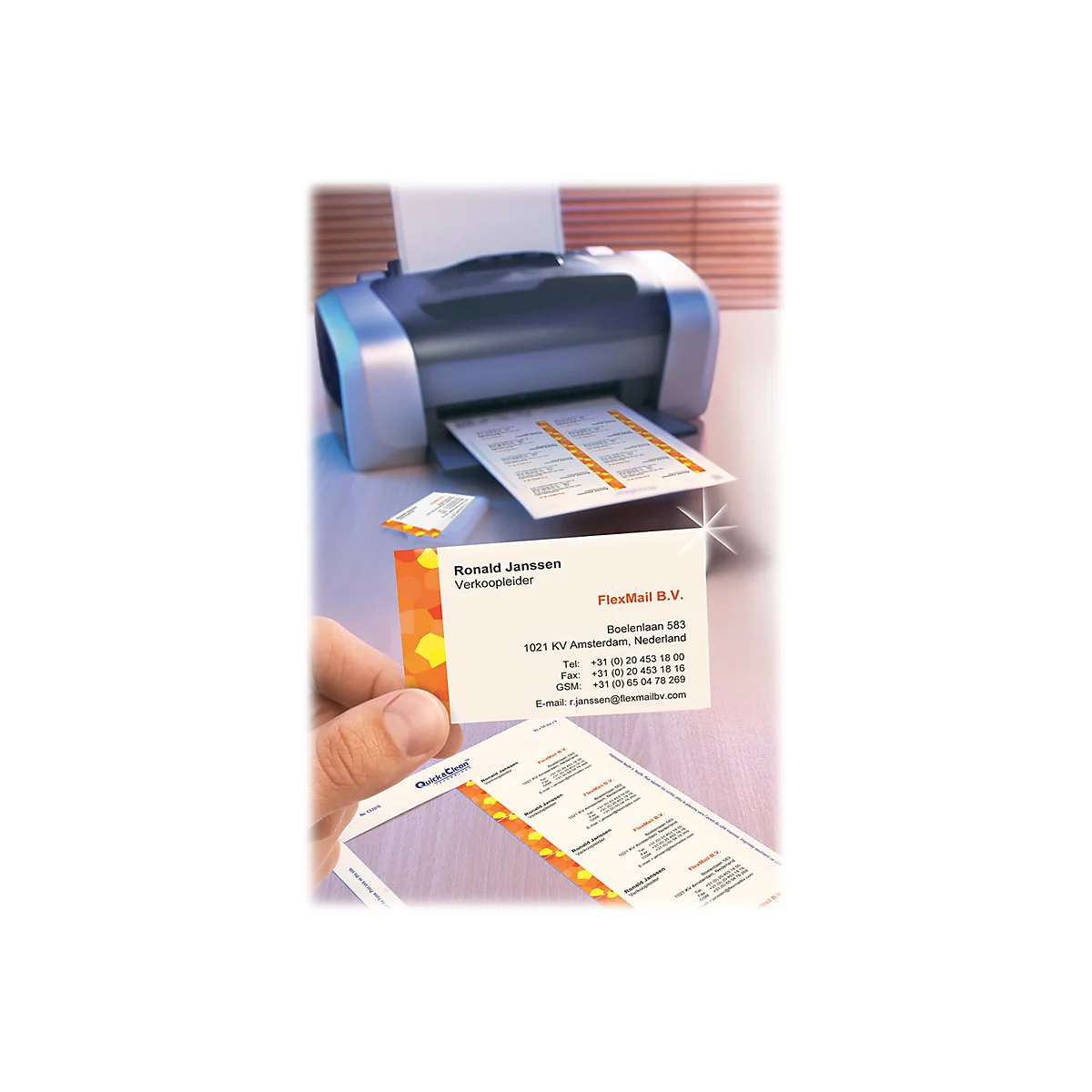 Hand hält bedruckte Visitenkarte neben einem Drucker mit einem Blatt vorgestanzter Etiketten.