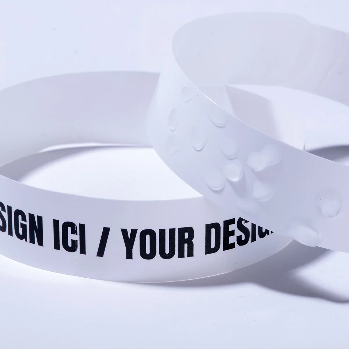 Weißes Armband mit der Aufschrift 'DESIGN ICI / YOUR DESIGN' und Wassertropfen als Zeichen für Wasserfestigkeit.