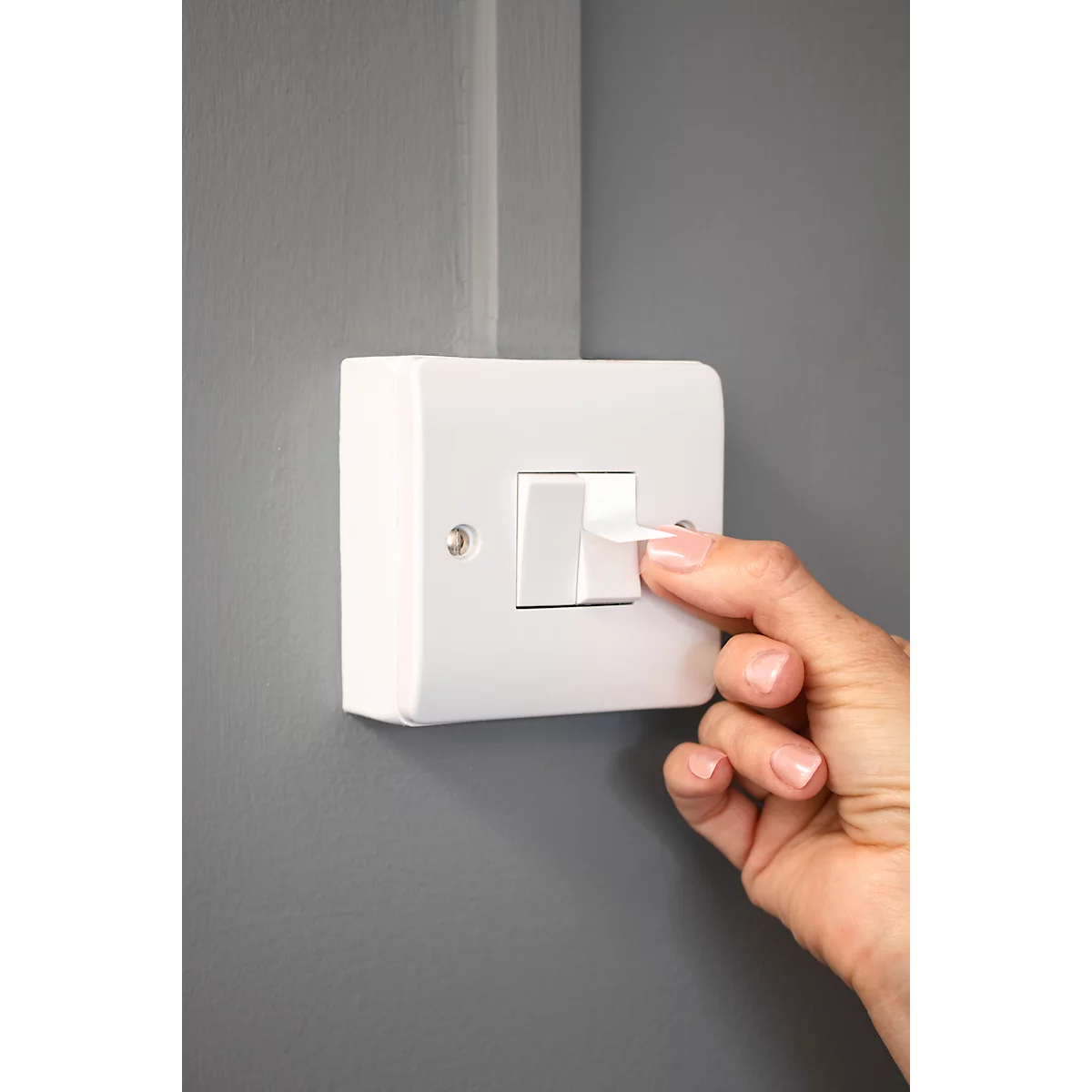 La main actionne un interrupteur sur un mur gris.