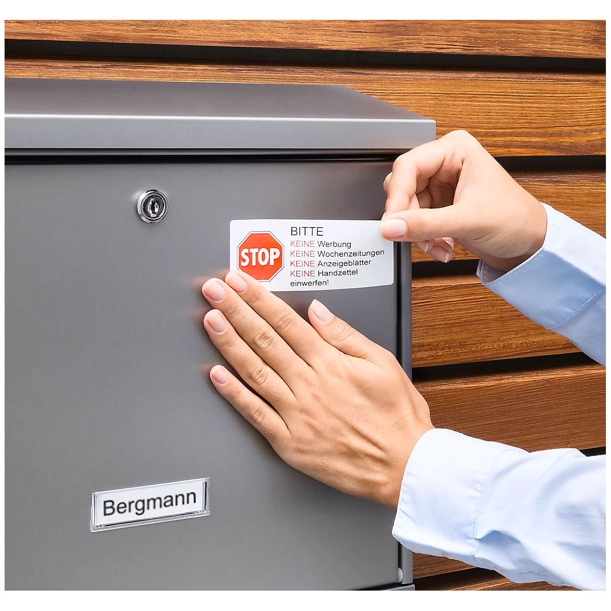 Person sticking a stop-advertising sticker on a mailbox. Sticker shows a red stop symbol, with 'Bitte' below.