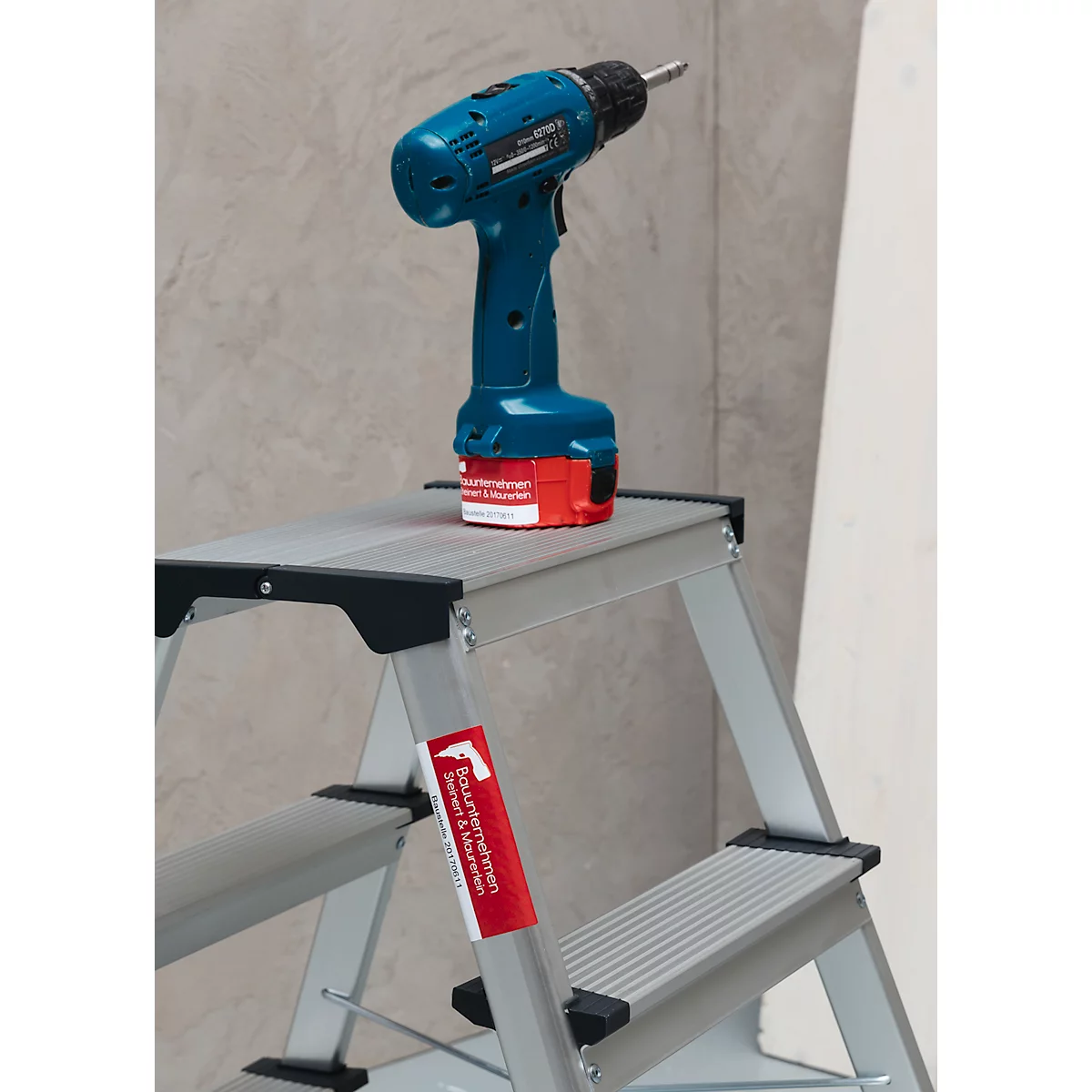 Blue cordless screwdriver on a silver stepladder. A red warning sign on the chair.