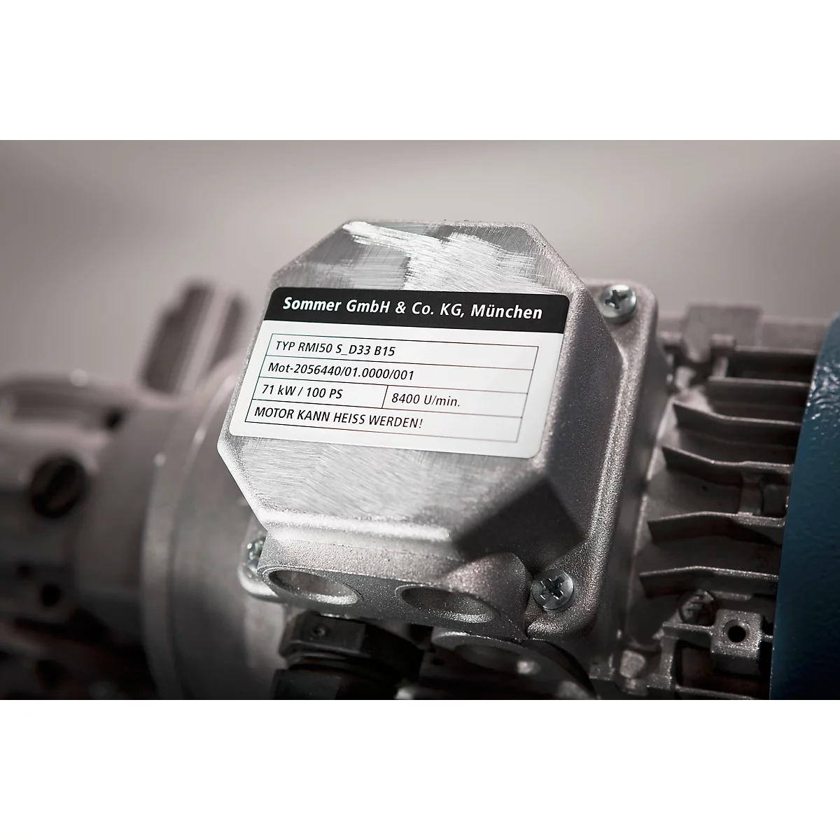 Close-up of a silver engine block with an information sticker. The sticker displays text: Sommer GmbH & Co. KG, München, and technical specifications.