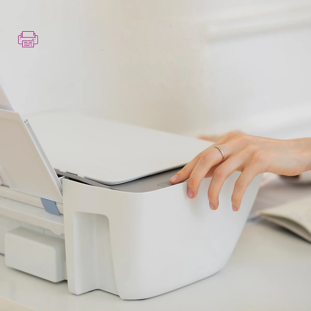 Een hand die een witte printer bedient op een licht bureau.