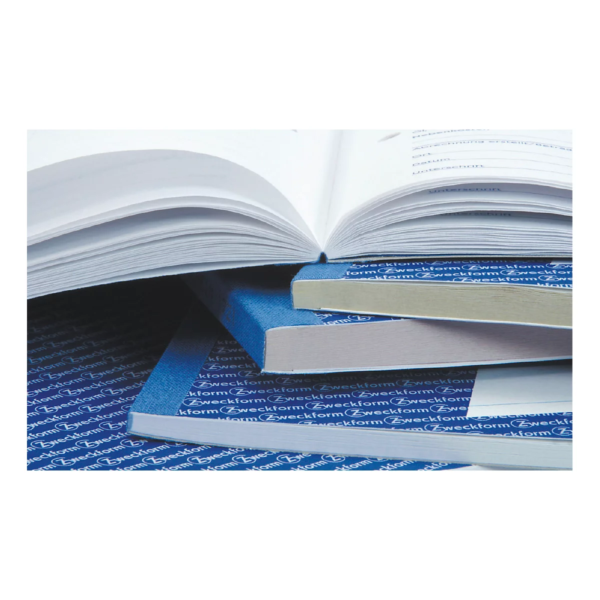 Close-up of books; open book, underneath stacked notepads with blue covers.