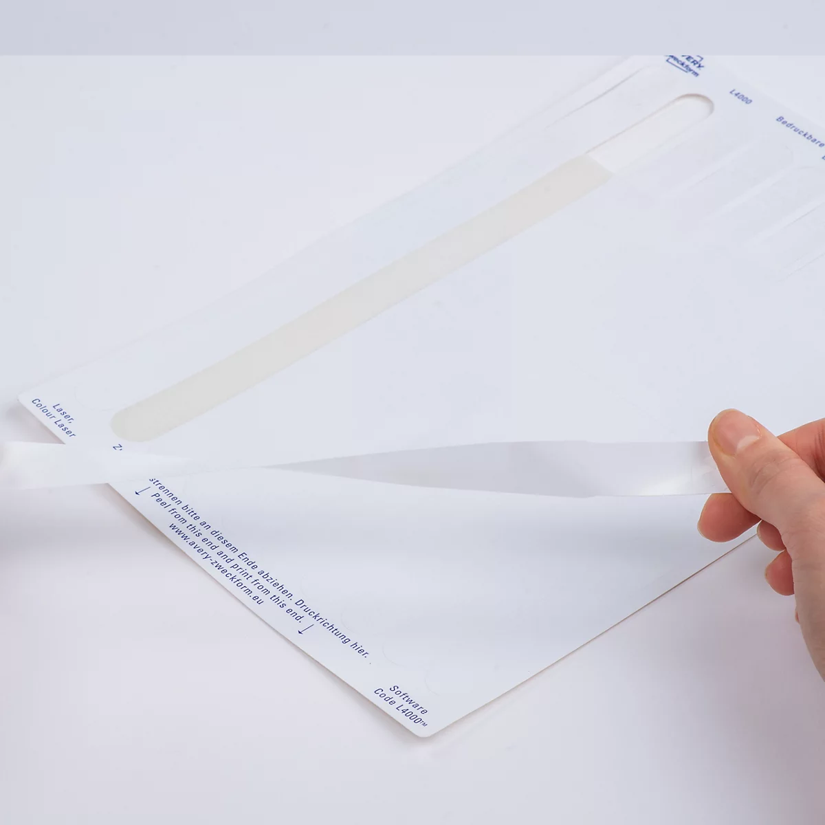Een hand trekt een witte kleefstrip van een stickervel. Tekst: SCHEURVAST. Ook voor meerdere dagen houdbaar.