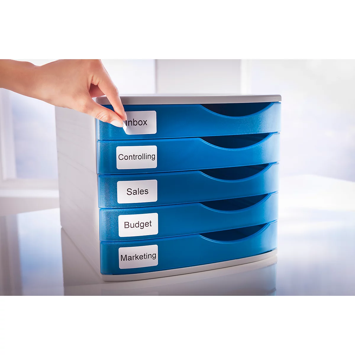 A hand places a label that reads "Inbox" on a blue document filing tray. Below are labels with: Controlling, Sales, Budget, Marketing.