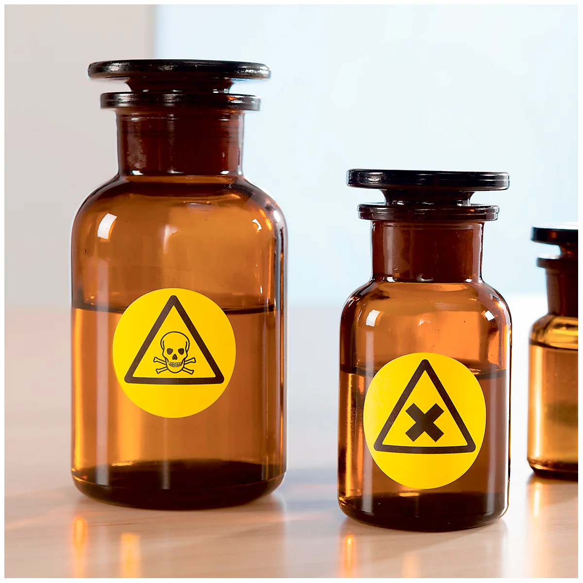 Two brown glass bottles with black lids and yellow warning signs. One shows a skull, the other a cross. Liquid is visible.