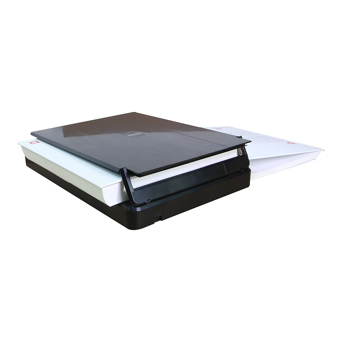 Ein schwarzer Flachbettscanner mit offenem Deckel, der auf einem weißen Hintergrund positioniert ist. Auf dem Scanner liegen mehrere Papierstapel.