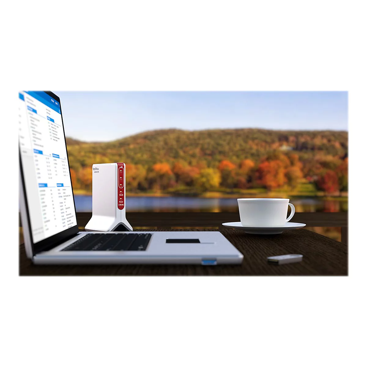 Ordinateur portable, routeur et tasse à café sur une table avec vue sur un lac et une forêt.