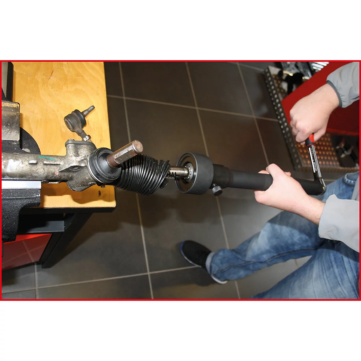 Ein Mechaniker montiert ein Teil an einer Lenkung. Er sitzt, hält Werkzeug in der Hand und schraubt.