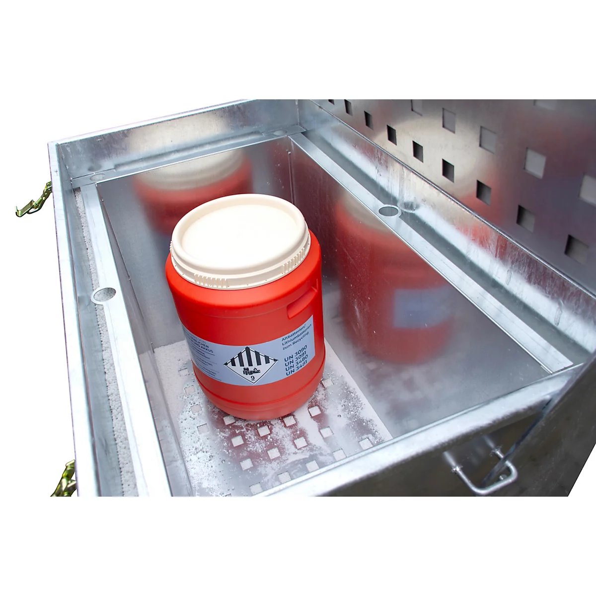 Récipient rouge pour matières dangereuses avec autocollants dans une boîte métallique.