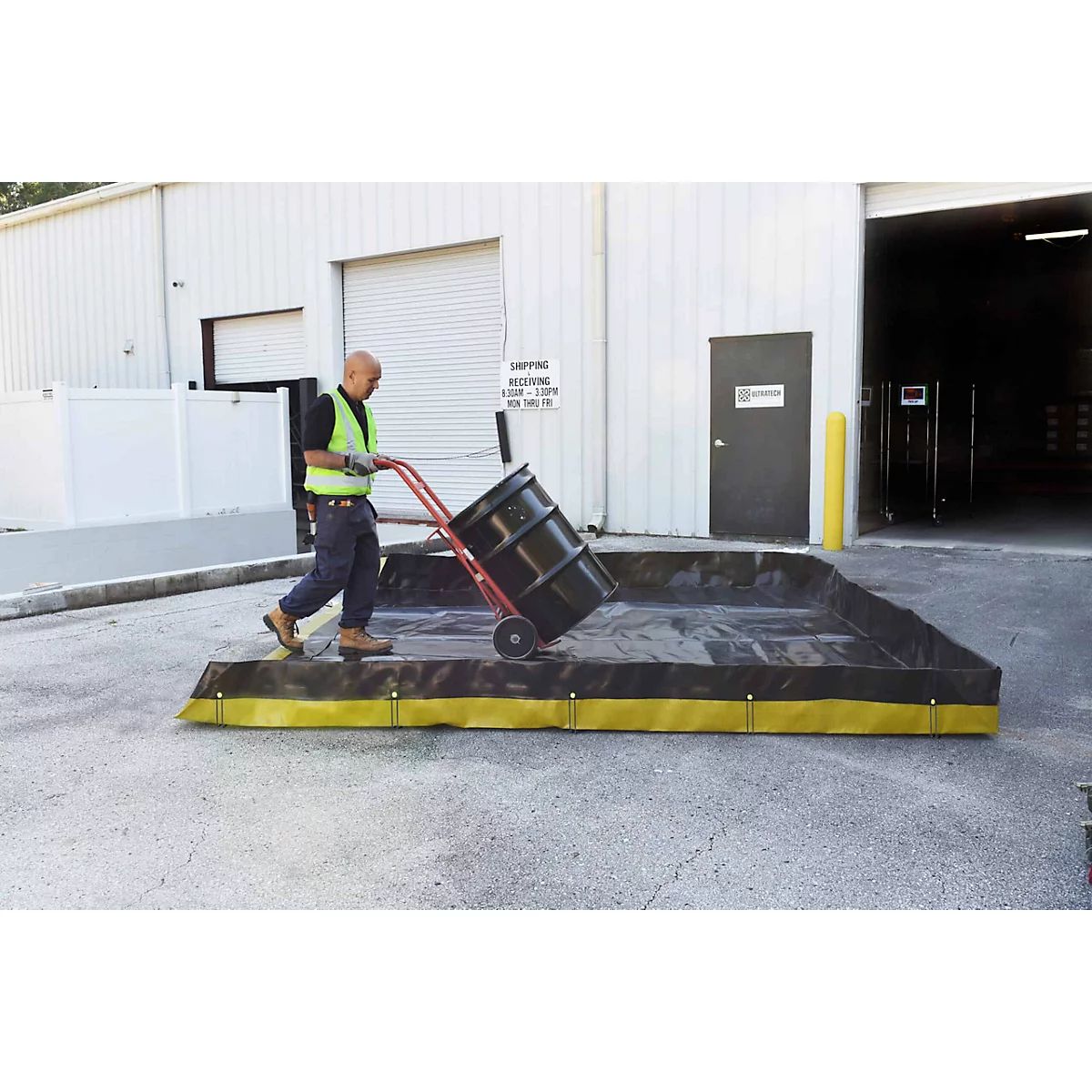 Un homme pousse un tambour avec un chariot dans un bac de rétention noir avec une bordure jaune.