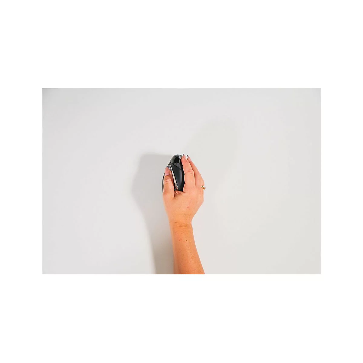 Eine Hand hält eine schwarze Computermaus auf weißem Hintergrund. Die Frau trägt einen goldenen Ring.